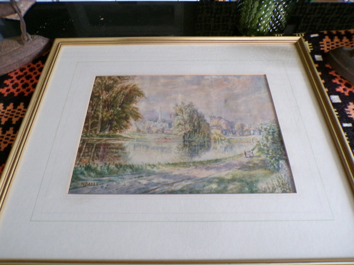 Framed W Bates watercolour of a lake and town scene.